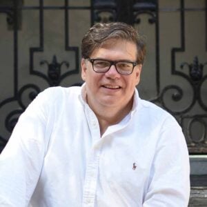 A man in a white shirt sitting on the stoop of a brownstone.