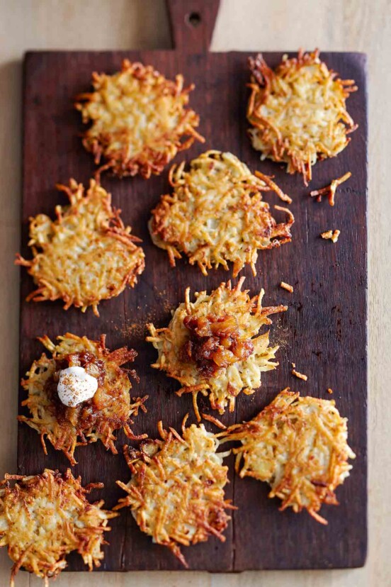 Nine potato latkes with apple-date chutney and cinnamon sour cream on a wooden cutting board.