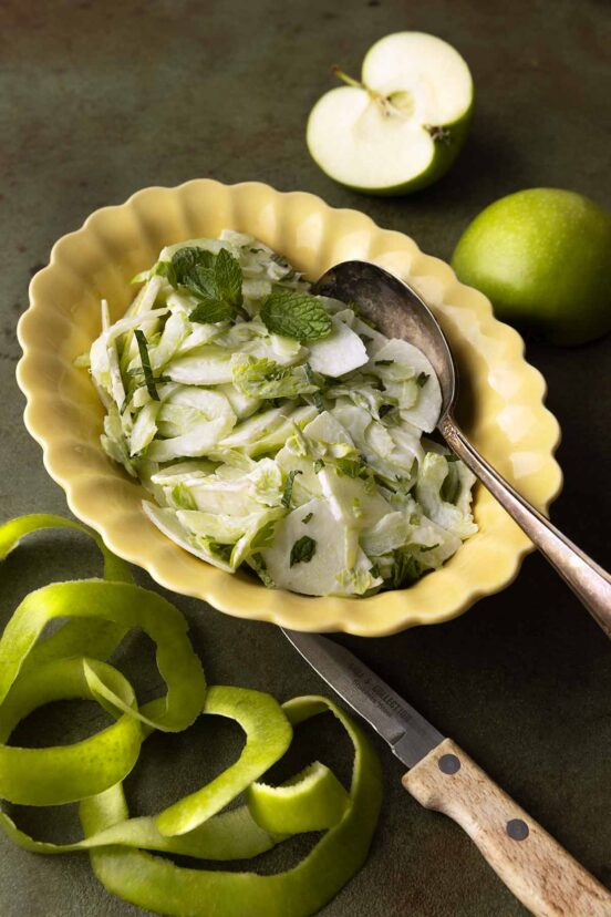 An apple and celery salad in a creamy dressing, garnished with mint leaves in a yellow scalloped bowl.