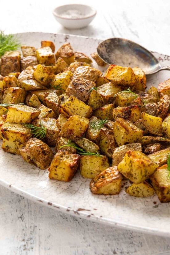 An oval platter filled with cubed roasted potatoes, garnished with fresh dill.