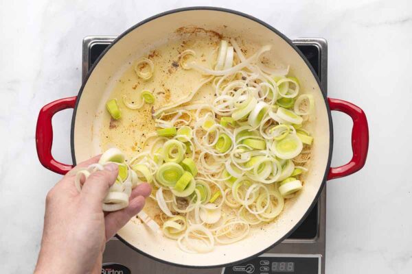 Sliced leeks being added to a skillet.