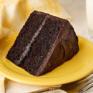 A slice of Hershey's chocolate cake with chocolate frosting on a yellow plate, with the remaining cake on a stand in the background.