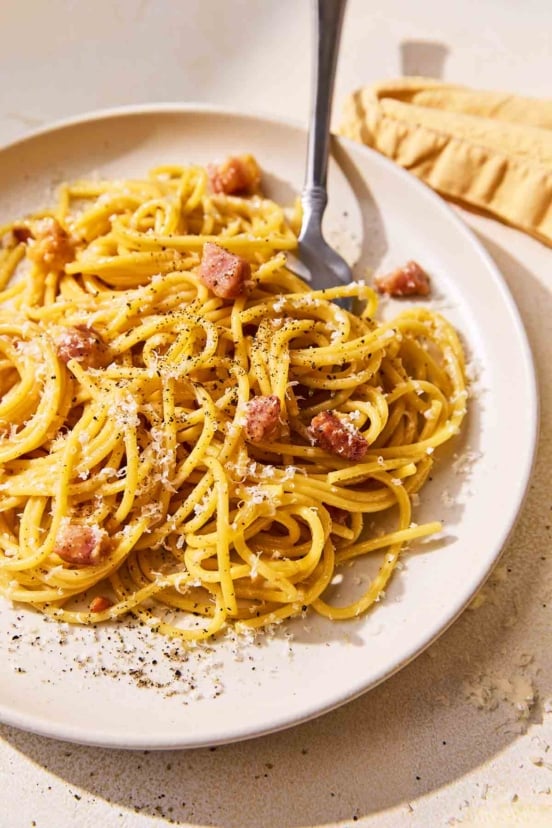 A plate of spaghetti carbonara with cubes of pancetta, Parmesan, and black pepper.