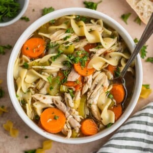 Overhead view of rotisserie chicken noodle soup in white bowl with spoon.