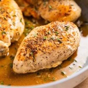 Seared chicken breast in skillet in buttery white wine sauce.