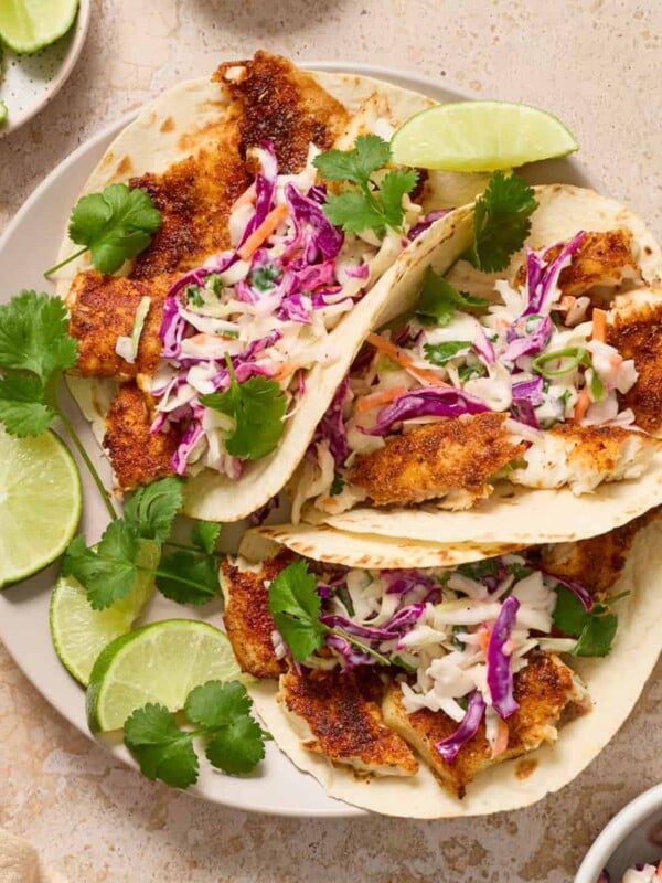 Air fryer fish tacos on white plate with lime and cilantro over top.