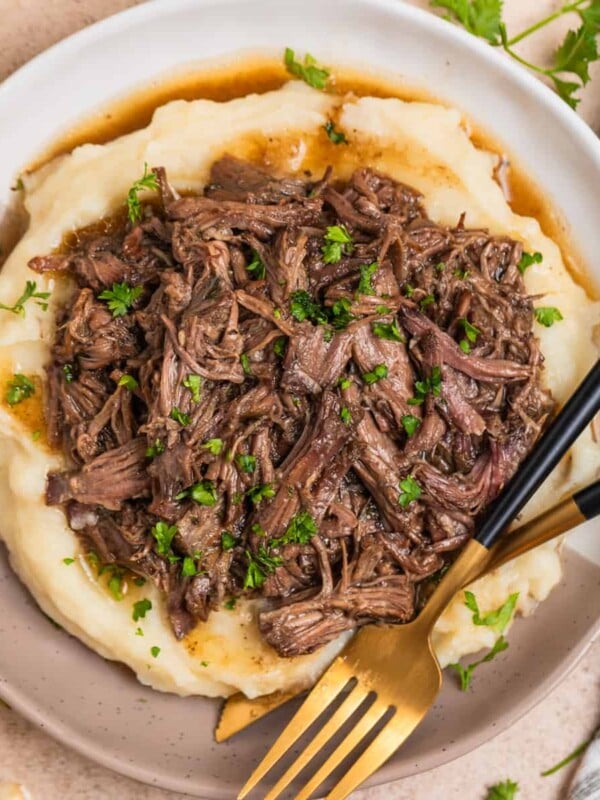 Tan and white plate with crock pot shredded beef over mashed potatoes.