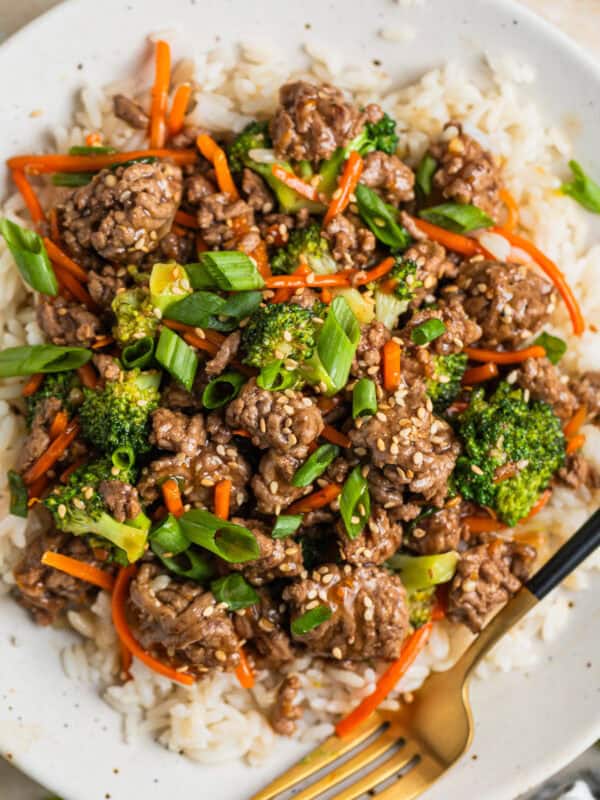 White plate with beef teriyaki served over white rice and topped with chopped green onions and toasted sesame seeds.