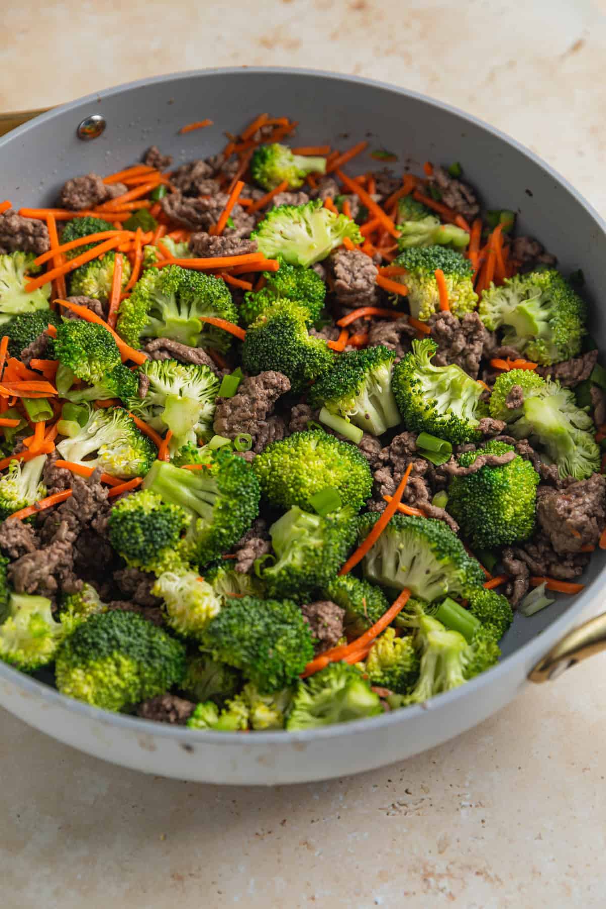 Fresh broccoli florets and shredded carrots added to skillet with browned ground beef.