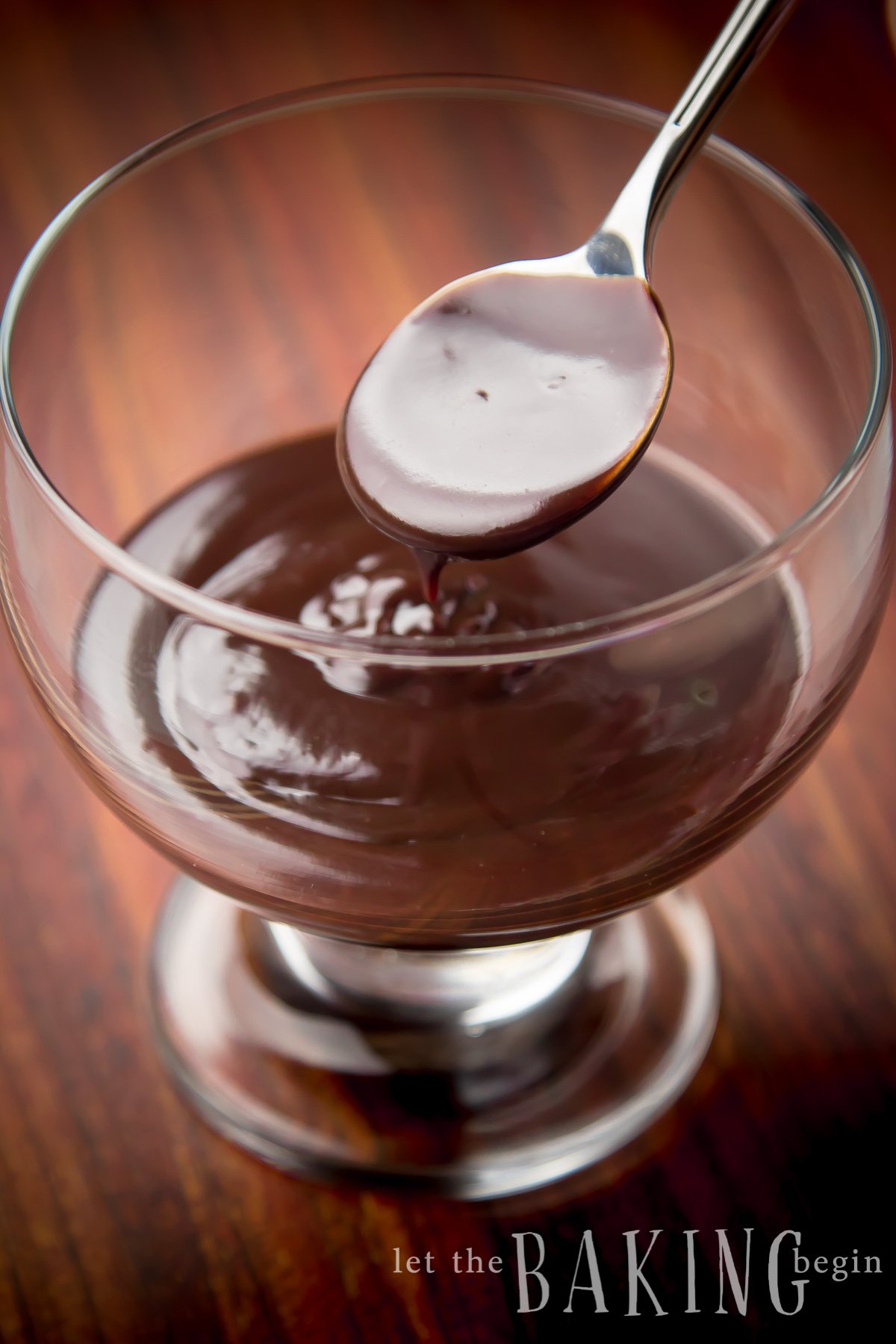 Rich chocolate ganache on a glass bowl with a spoonful of ganache.