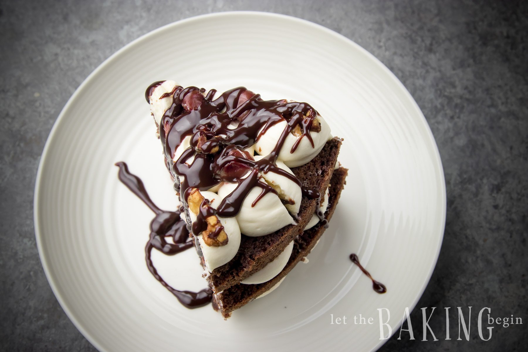 Chocolate cake on a white plate topped with extra shiny chocolate ganache.