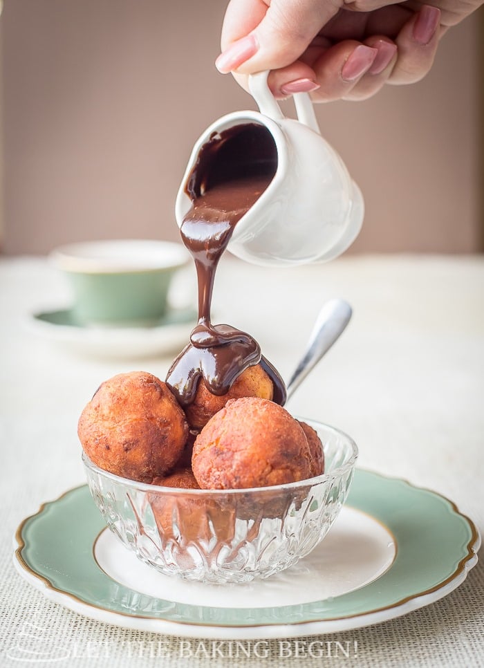 Donuts in a glass bowl on a green and white decorative plate being poured with a chocolate ganache. 