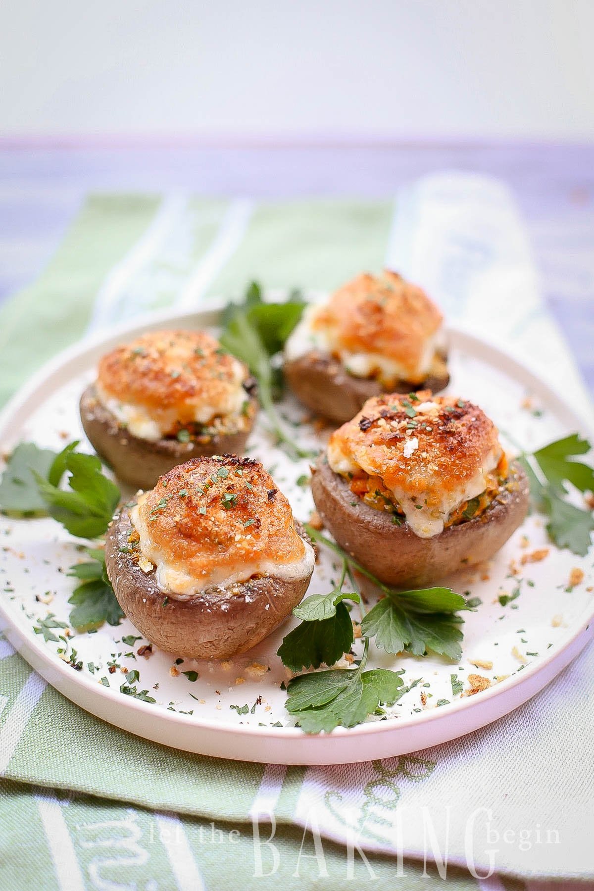 Four cheesy stuffed mushrooms topped with fresh greens on a white tray.