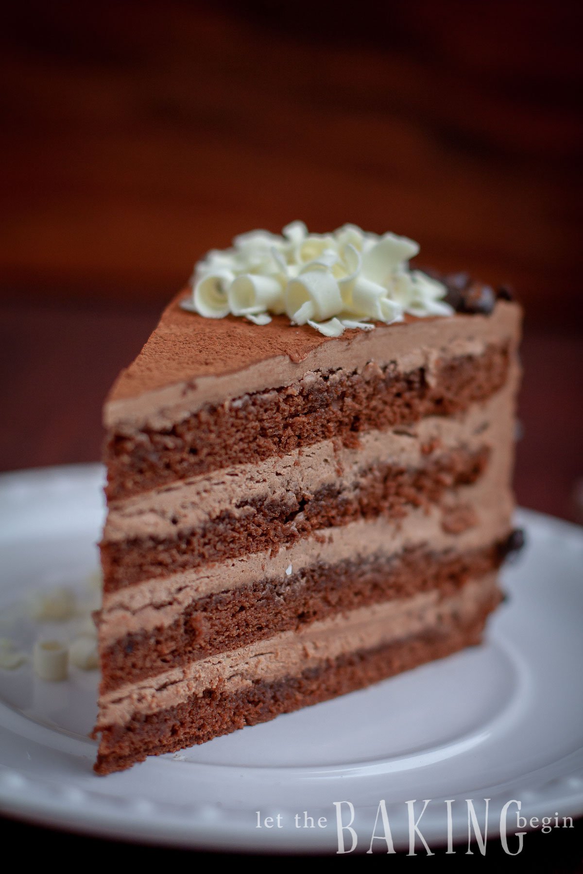 Slice of prague cake topped with rolled white chocolate on a white decorative plate.