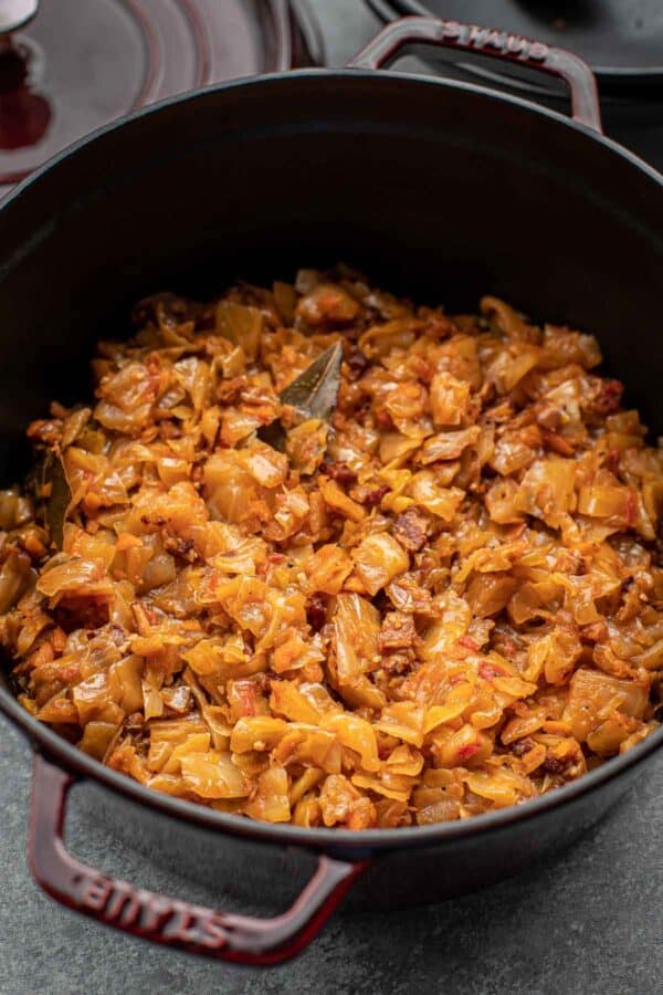 Braised cabbage with bacon in a burgundy dutch oven, overhead shot. 