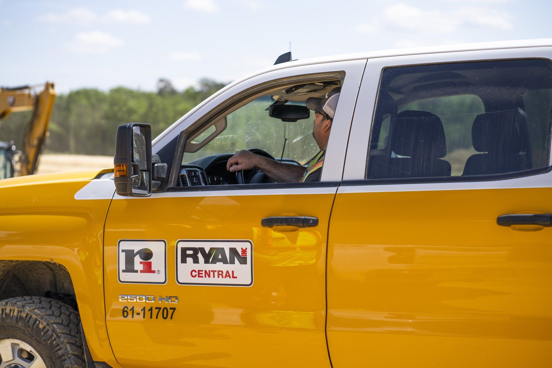 A man is driving a yellow truck on a construction site.