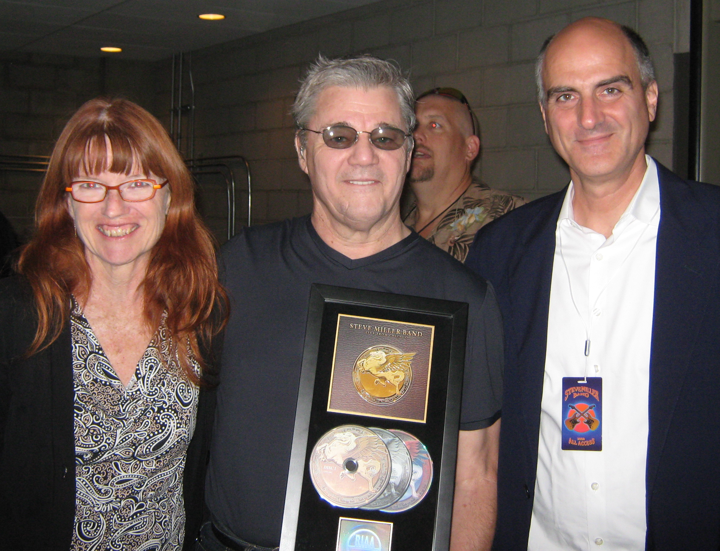 Judi Kerr, PR  and Jack Gulick, Producer present Steve Miller with RIAA - Certified Gold Plaque Award for Steve Miller "Live In Chicago" The DVD debuted at #1  on the Billboard's Top Music Video Chart. 