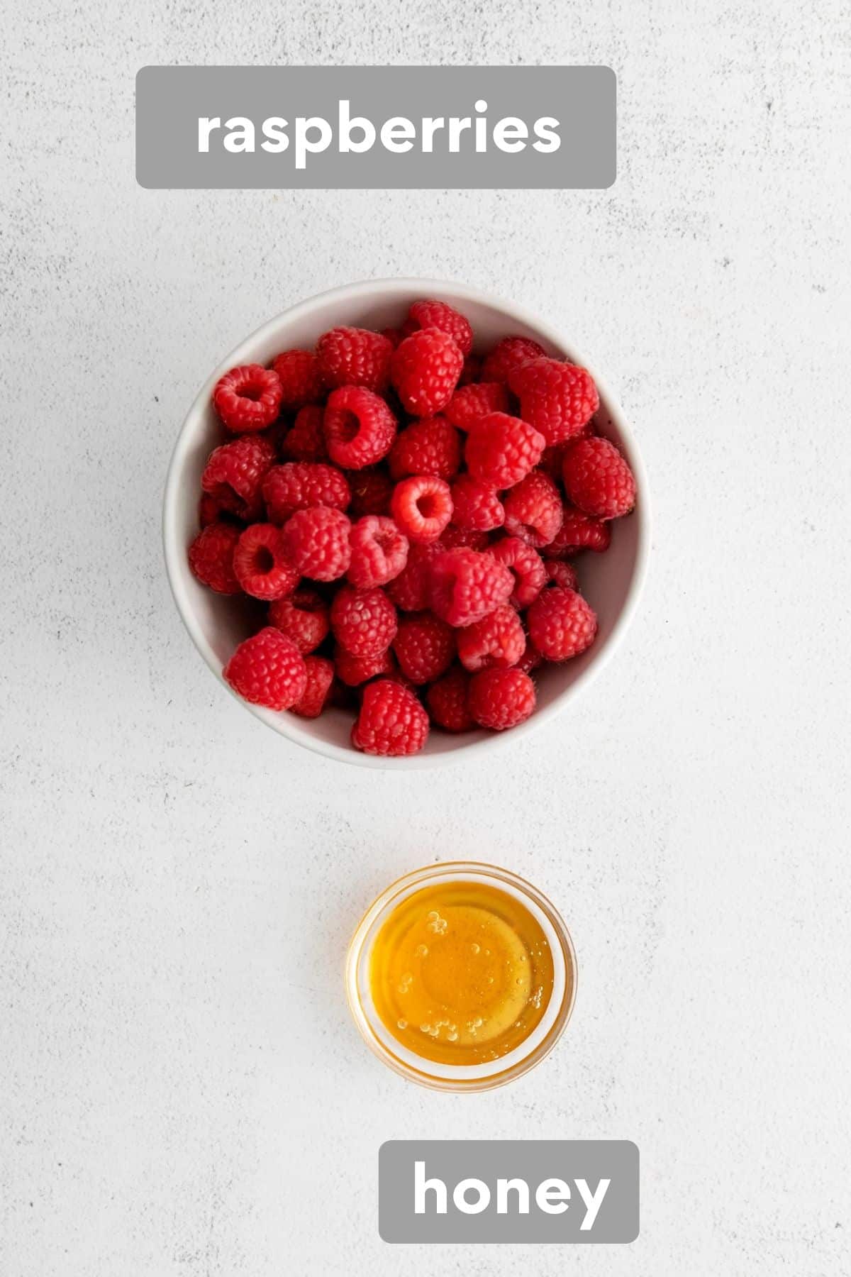 A bowl of fresh raspberries next to a small bowl of honey