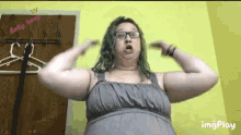 a woman with green hair and glasses is flexing her arms in front of a yellow wall .