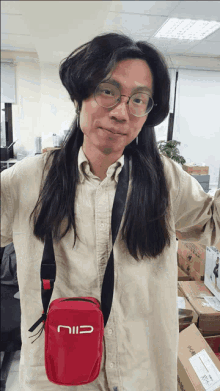 a man with long hair is wearing glasses and carrying a red bag that says cili