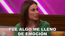 a woman in a green shirt is sitting on a couch with a purple background and says fue algo me lleno de emocion .