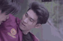 two young men are standing next to each other and one of them is wearing a purple jacket with a badge on it .