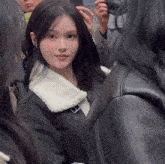 a woman wearing a black jacket with a white collar looks at the camera