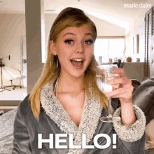 a woman in a bathrobe holds a glass of wine and says hello in the corner