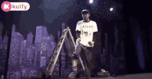 a man is standing on a stage with a ladder in front of a city skyline .
