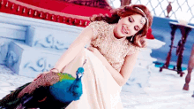 a woman in a white dress is holding a peacock on her lap