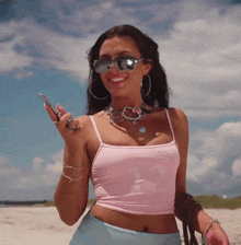 a woman wearing sunglasses and a pink top is standing on the beach