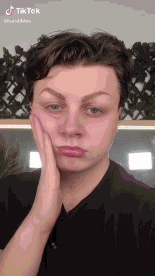 a young man is making a funny face with his hand on his face while a tiktok video is playing in the background