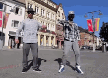 two men are dancing on a street in front of a building with a flag on it