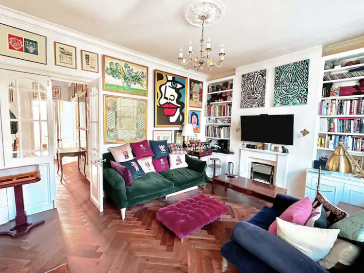 Artsy living room with walls line with framed artwork, two sofas and an ottoman. 