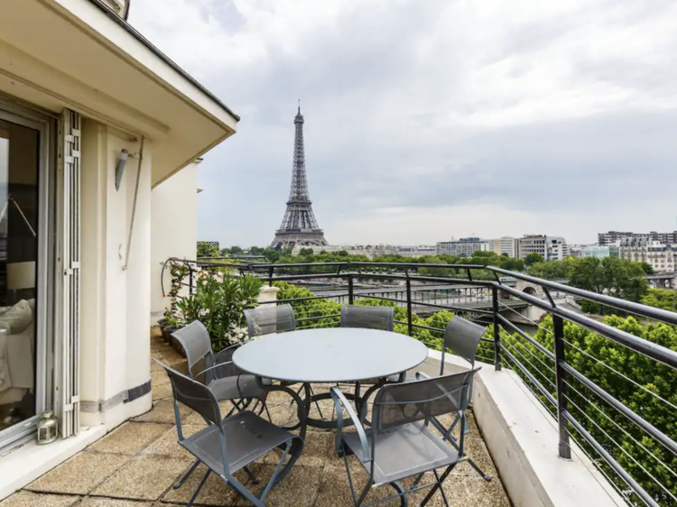 exterior shot from one of Paris's best Airbnbs, with the Eiffel Tower on the horizon, and a little round table with a number of chairs on the balcony.