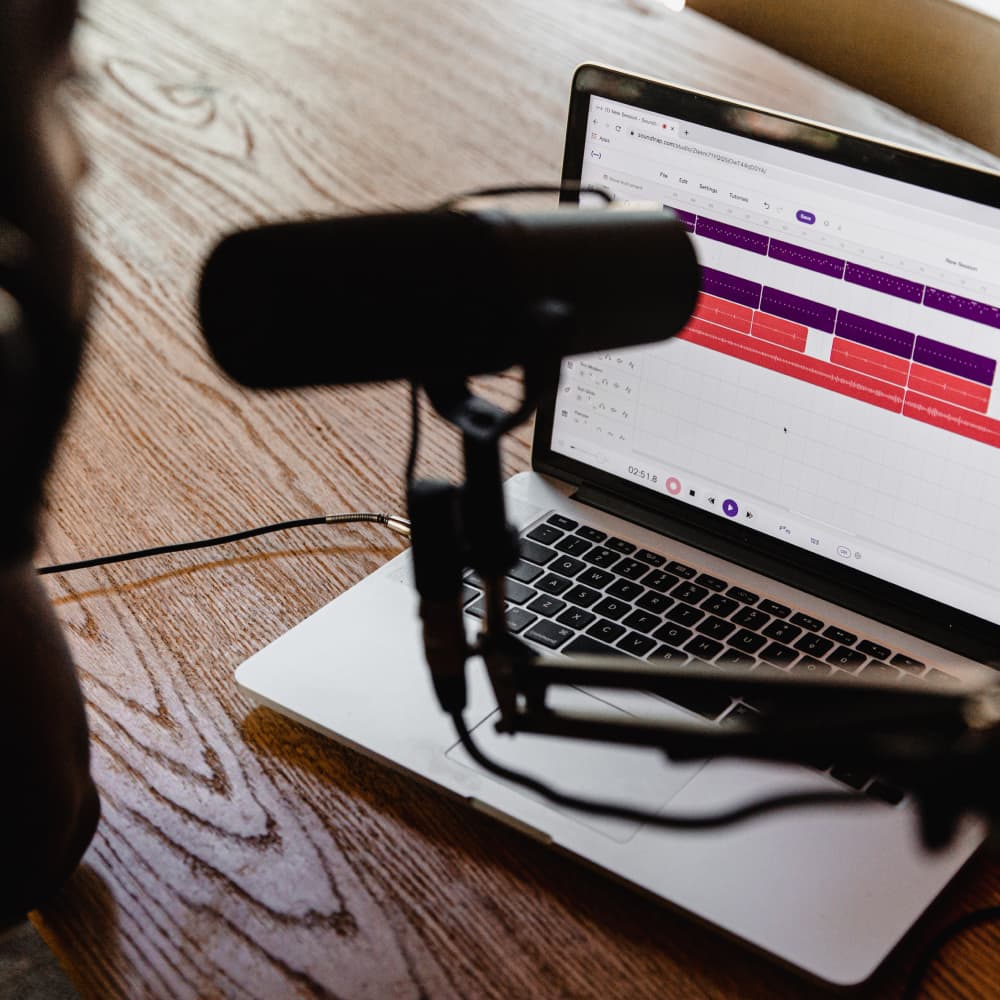 Podcast microphone with computer on wooden desk.