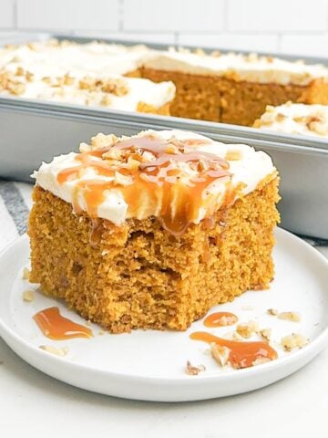 pumpkin pie bar with cream cheese frosting, walnuts, and caramel sauce on a white plate