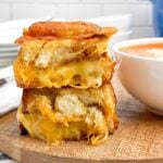 stack of oven grilled cheese sandwiches on a cutting board next to a bowl of tomato soup.