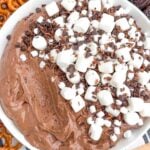 hot cocoa dip topped with marshmallows, chocolate chips and chocolate shavings in a white bowl.