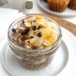 banana chia overnight oats in a mason jar topped with sliced bananas, almonds, chocolate chips, and honey.