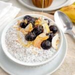 yogurt chia pudding in a white bowl topped with blueberries, coconut, cinnamon, and honey.