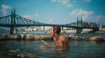 Person swimming in river with a bridge and cityscape in the background.