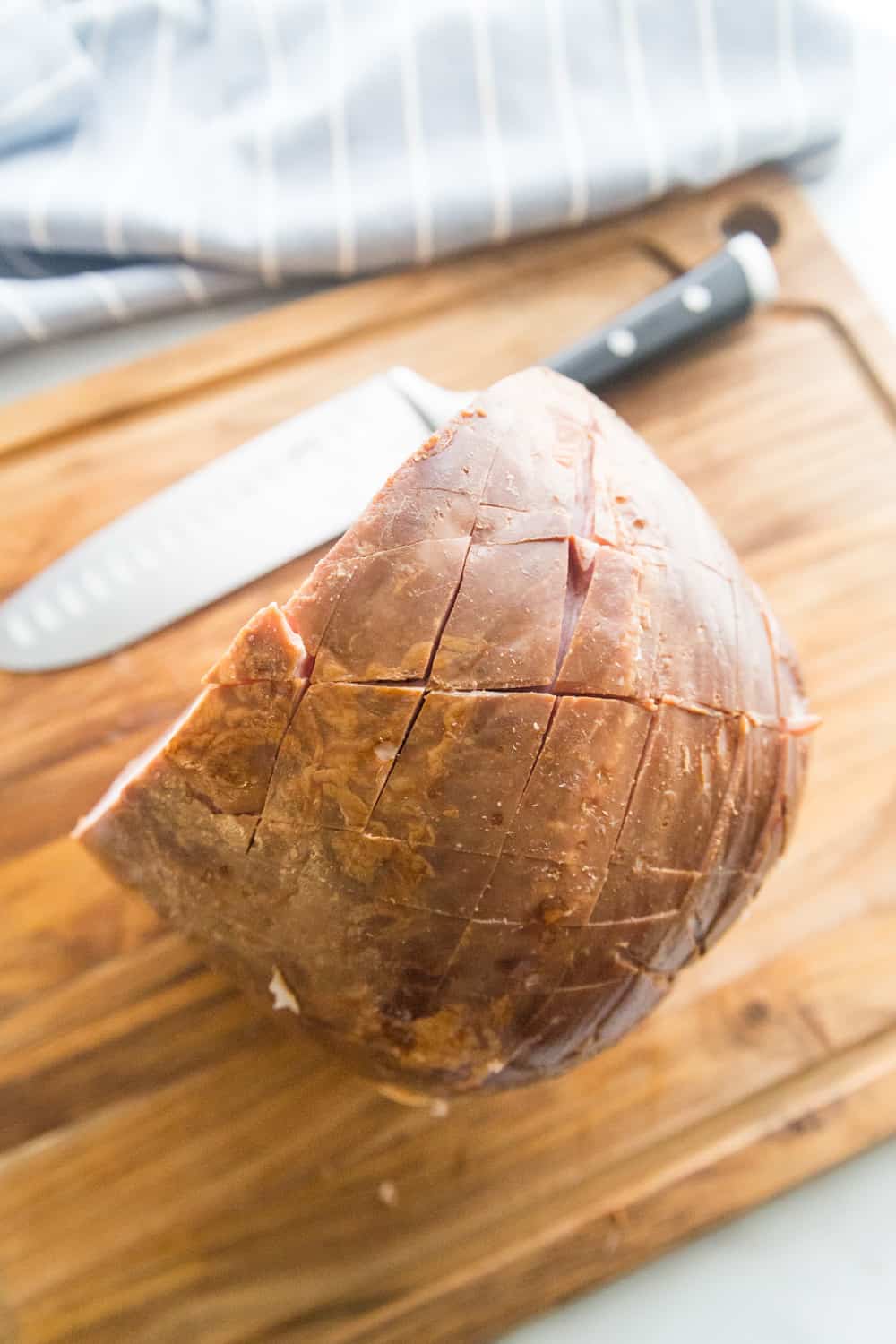 a scored ham sitting on a bamboo cutting board next to a knife