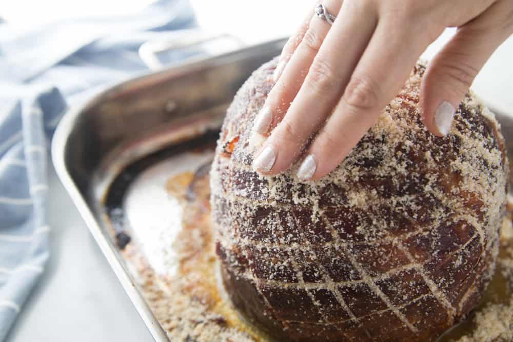 rubbing sugar rub on glazed ham sitting on a cookie sheet