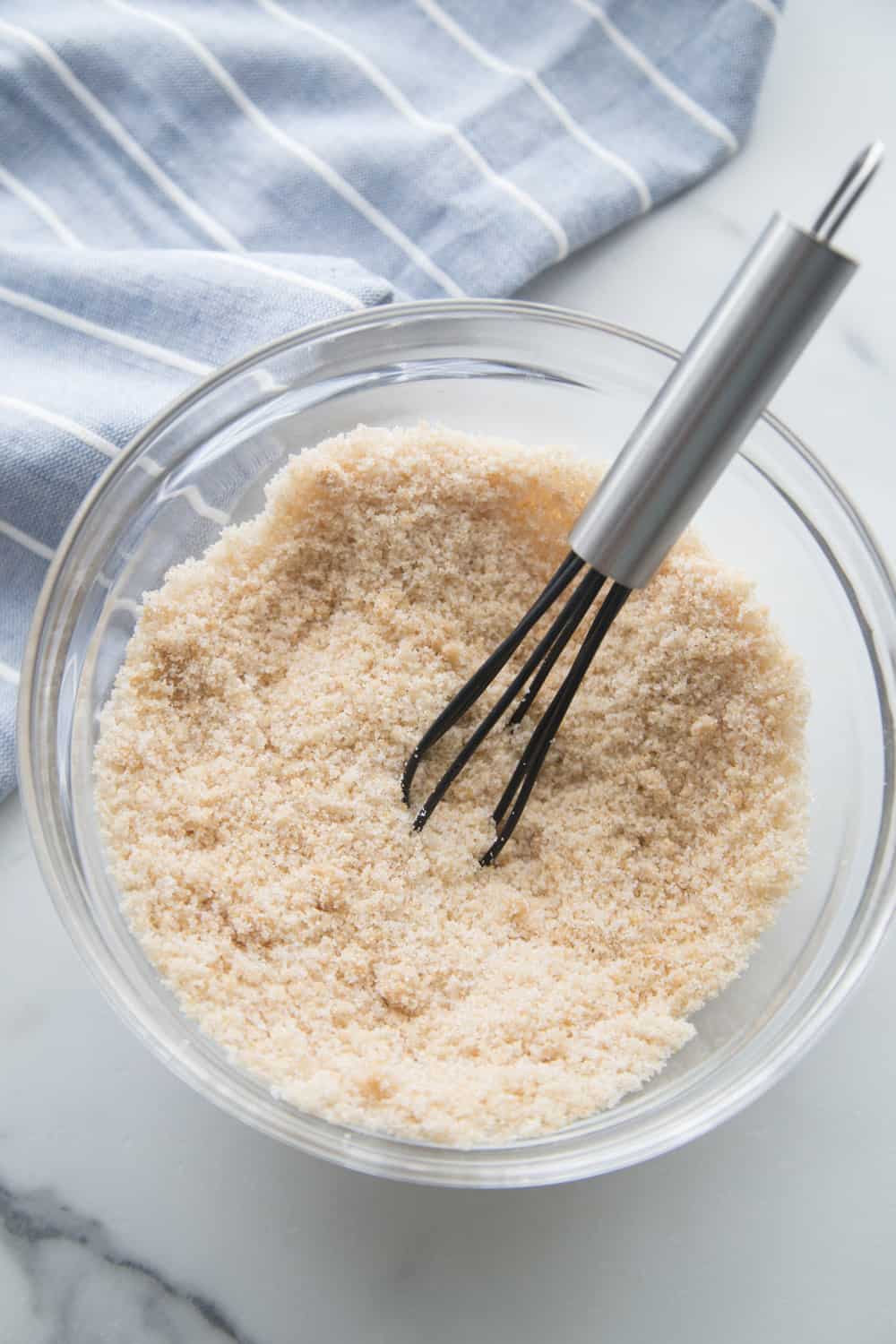 sugar rub in glass bowl on white counter, with a whisk in the bowl, and a tea towel in the top left corner