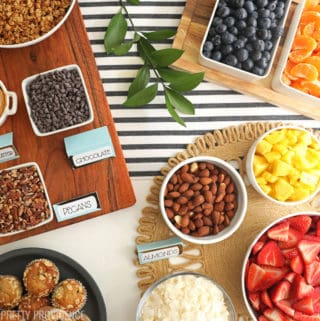 Yogurt Toppings on a table for brunch bar, granola, coconut, strawberries, blueberries, oranges, pineapple, kiwi.