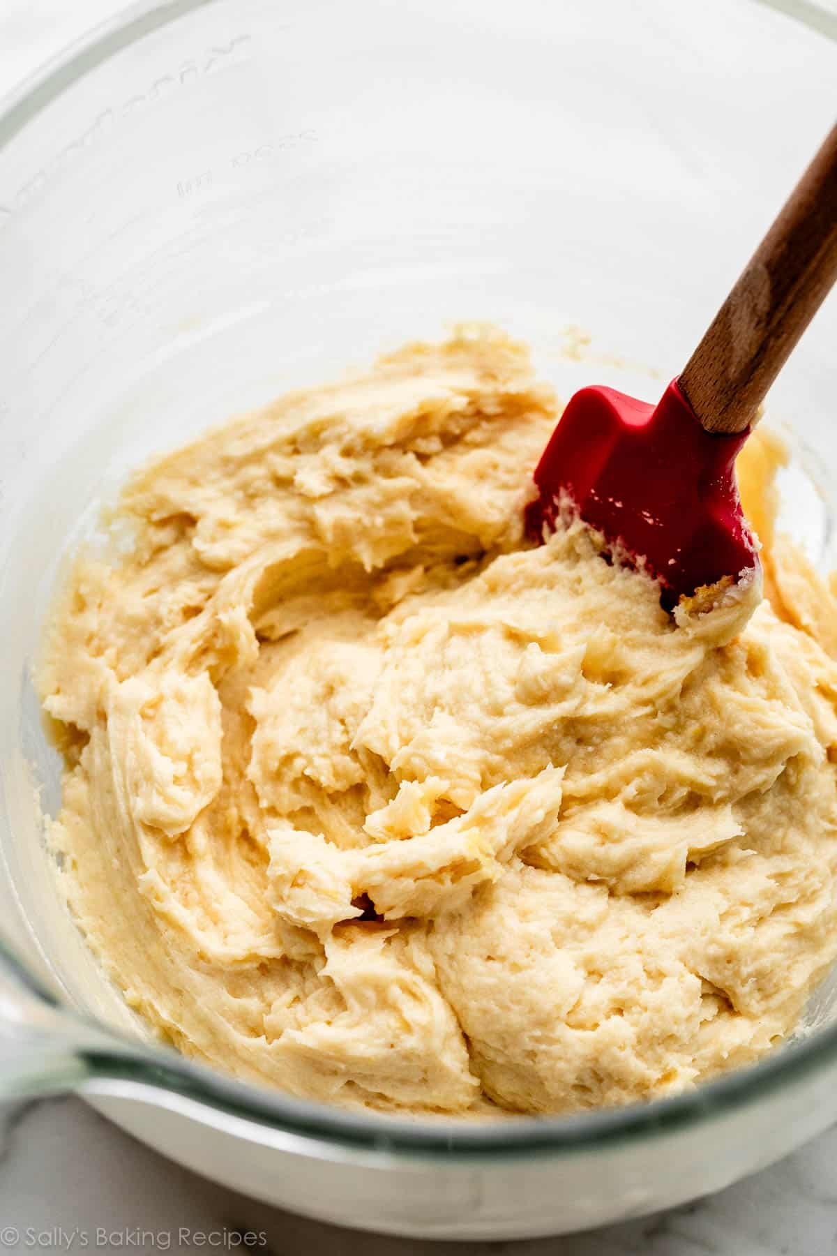 thick yellow batter in glass bowl with red spatula.