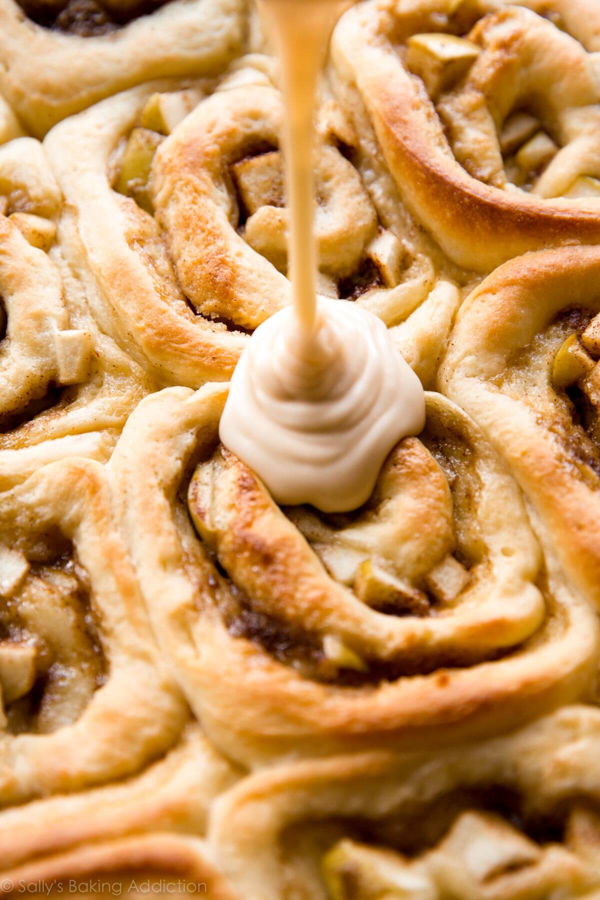 drizzling caramel icing onto apple cinnamon rolls