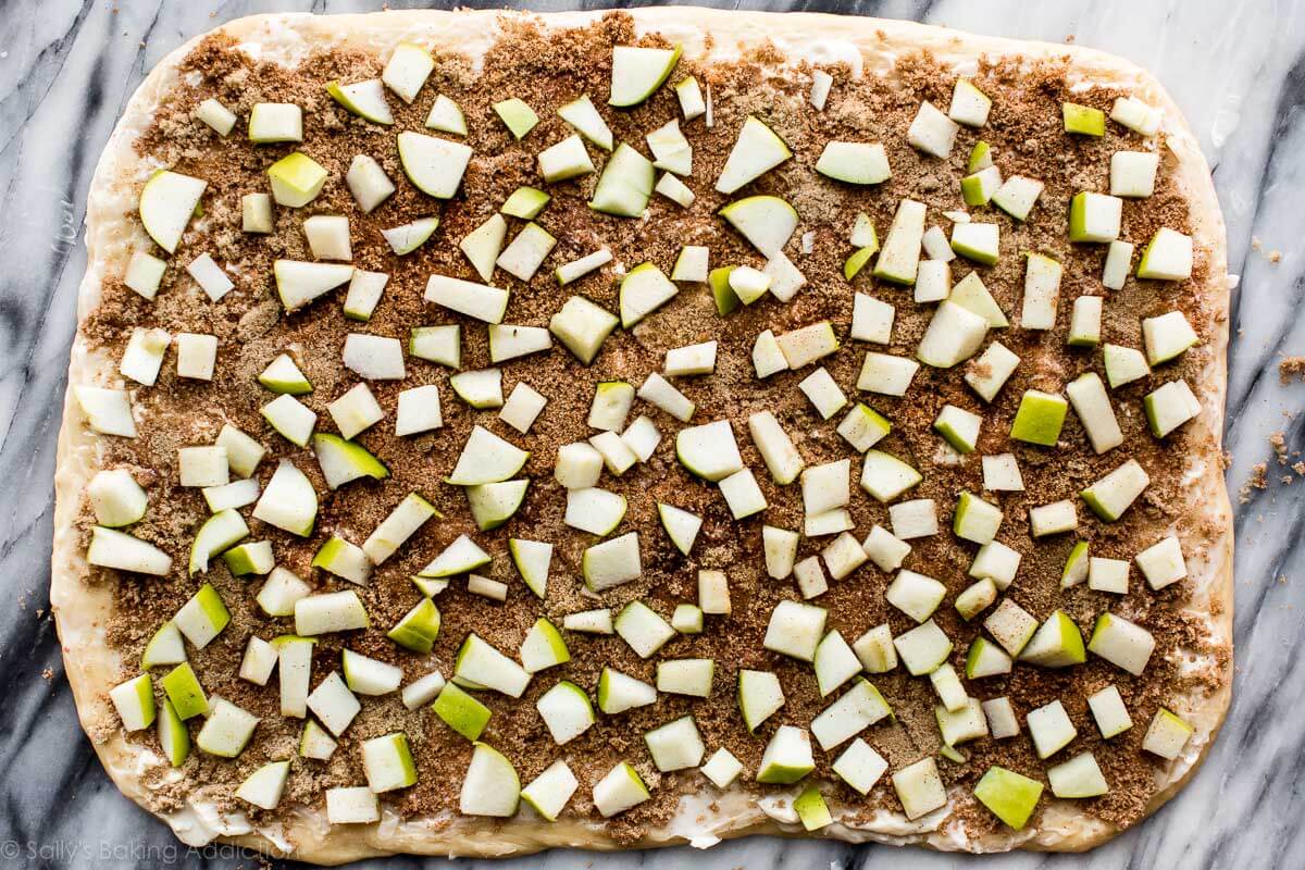 cinnamon roll dough rolled into a rectangle topped with cinnamon filling and chopped apples