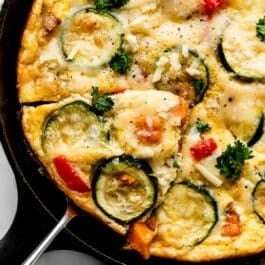 vegetable frittata in cast iron skillet with slice being removed.